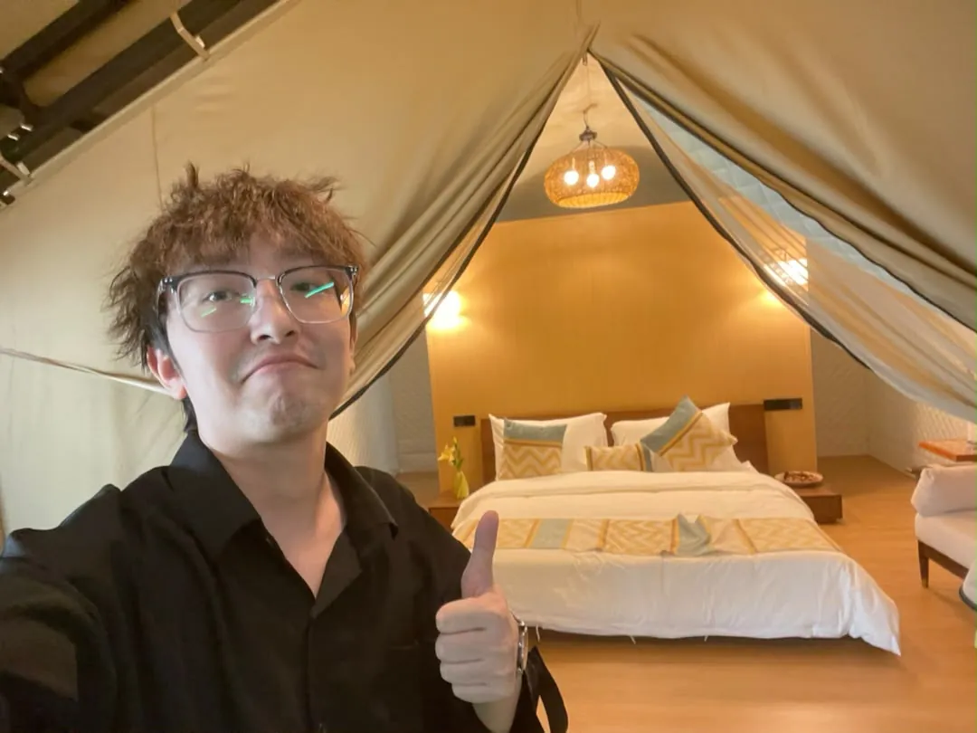 The author giving a thumbs-up inside a tent-style suite with a bed and a woven pendant lamp